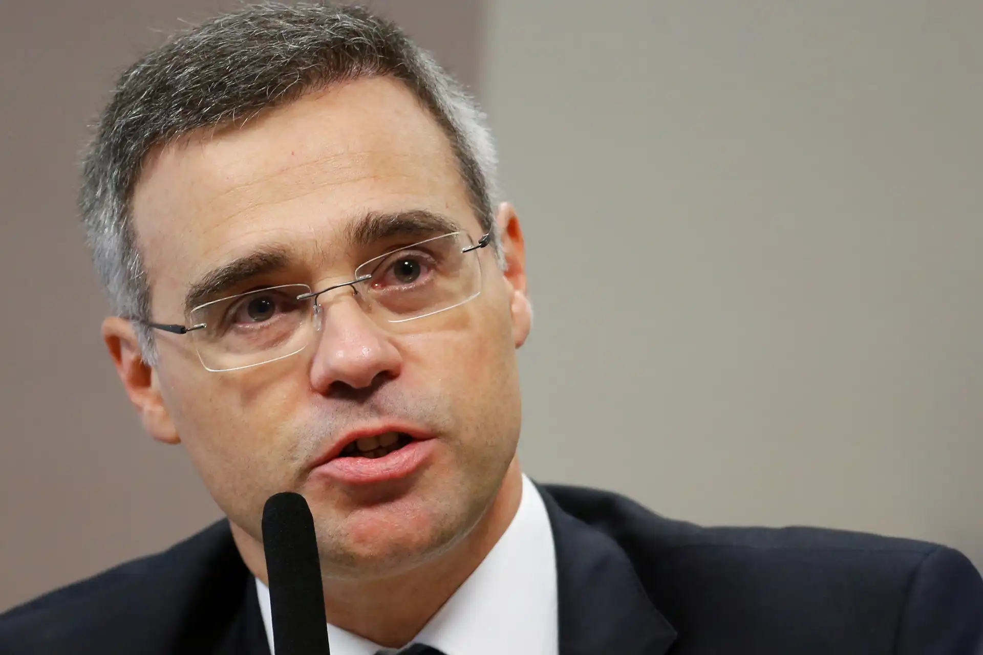 Homem de terno e óculos falando ao microfone em uma entrevista ou reunião, imagem otimizada para a palavra-chave.