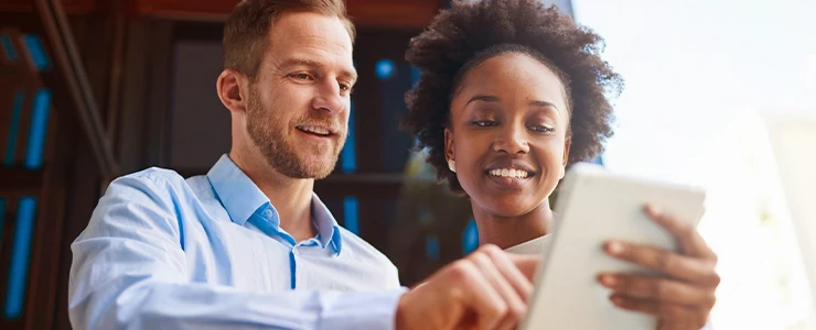 Homem e mulher de negócios sorrindo enquanto olham para um tablet, em um ambiente de escritório, com foco na colaboração tecnologia e publicidade