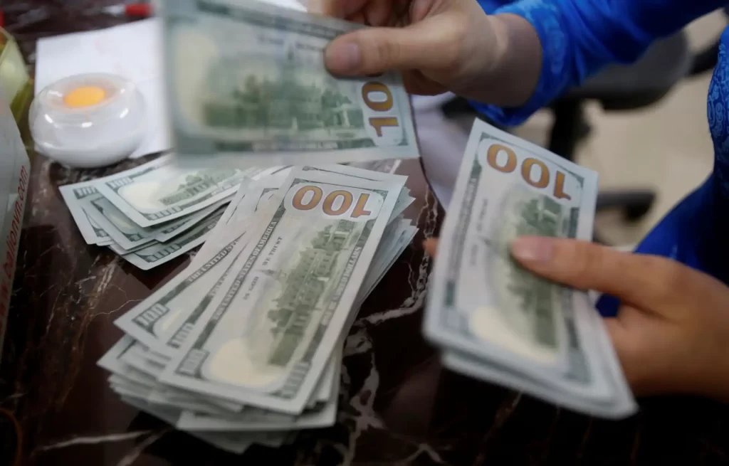 Pessoa manuseando várias cédulas de 100 dólares, detalhes visíveis, dinheiro em destaque.