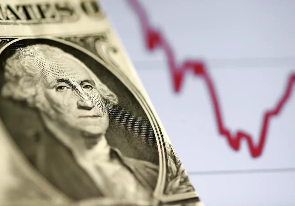 Imagem de uma nota de dólar com uma linha de gráfico vermelho de queda ao fundo, representando a volatilidade do mercado financeiro.