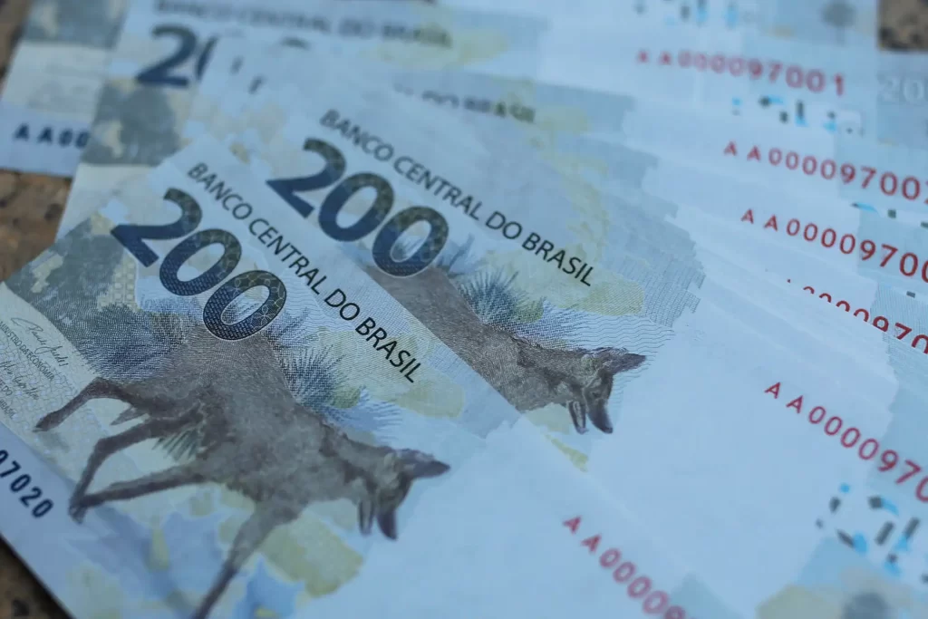 Notar uma nota de 200 reais do Banco Central do Brasil em destaque, cheia de detalhes e cores vibrantes, com outras cédulas ao fundo.