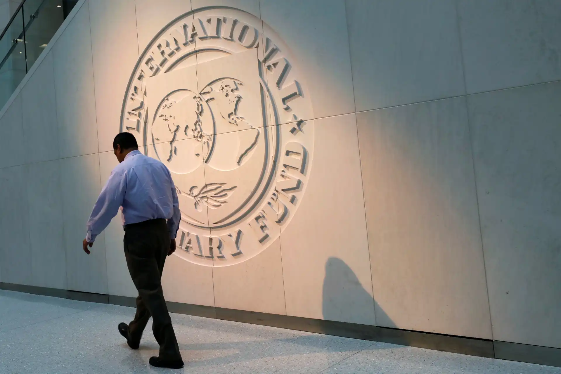 Homem de terno caminhando ao lado da logo da Organização das Nações Unidas (ONU) em um edifício internacional, simbolizando a diplomacia e cooperação global.