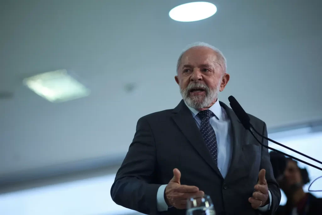 Retrato de um político idoso de cabelo branco e barba, usando terno e gravata, falando em um discurso ou palestra em ambiente interno bem iluminado.