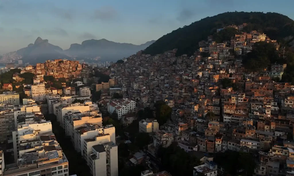 Vista de uma área urbana em uma colina com muitos prédios residenciais compactados, em uma manhã ou fim de tarde com névoa nas montanhas ao fundo.