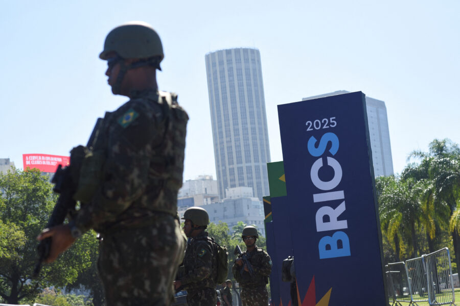 Soldados das forças armadas do Brasil durante evento oficial com o monumento Brasil 2025 ao fundo, cenário urbano de uma cidade brasileira.