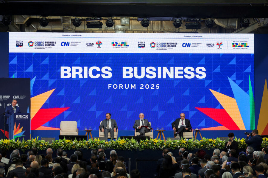 Pessoas participando do BRICS Business Forum 2025 com grande público presente, painel no palco com painelistas discutindo negócios internacionais.