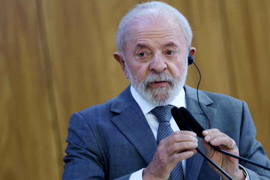 Homem de terno azul, com cabelo branco e barba grisalha, falando em um microfone durante uma apresentação ou discurso, em um ambiente de sala de reunião ou conferência.