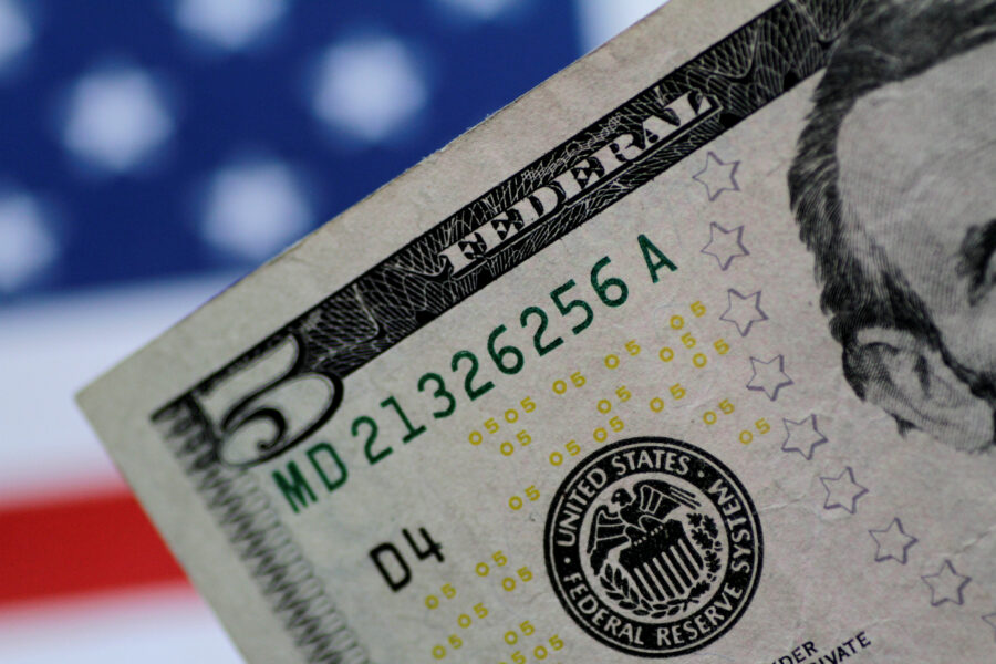 Imagem de uma nota de cinco dólares dos Estados Unidos com foco na parte superior, mostrando detalhes do valor e do símbolo do Federal Reserve System.