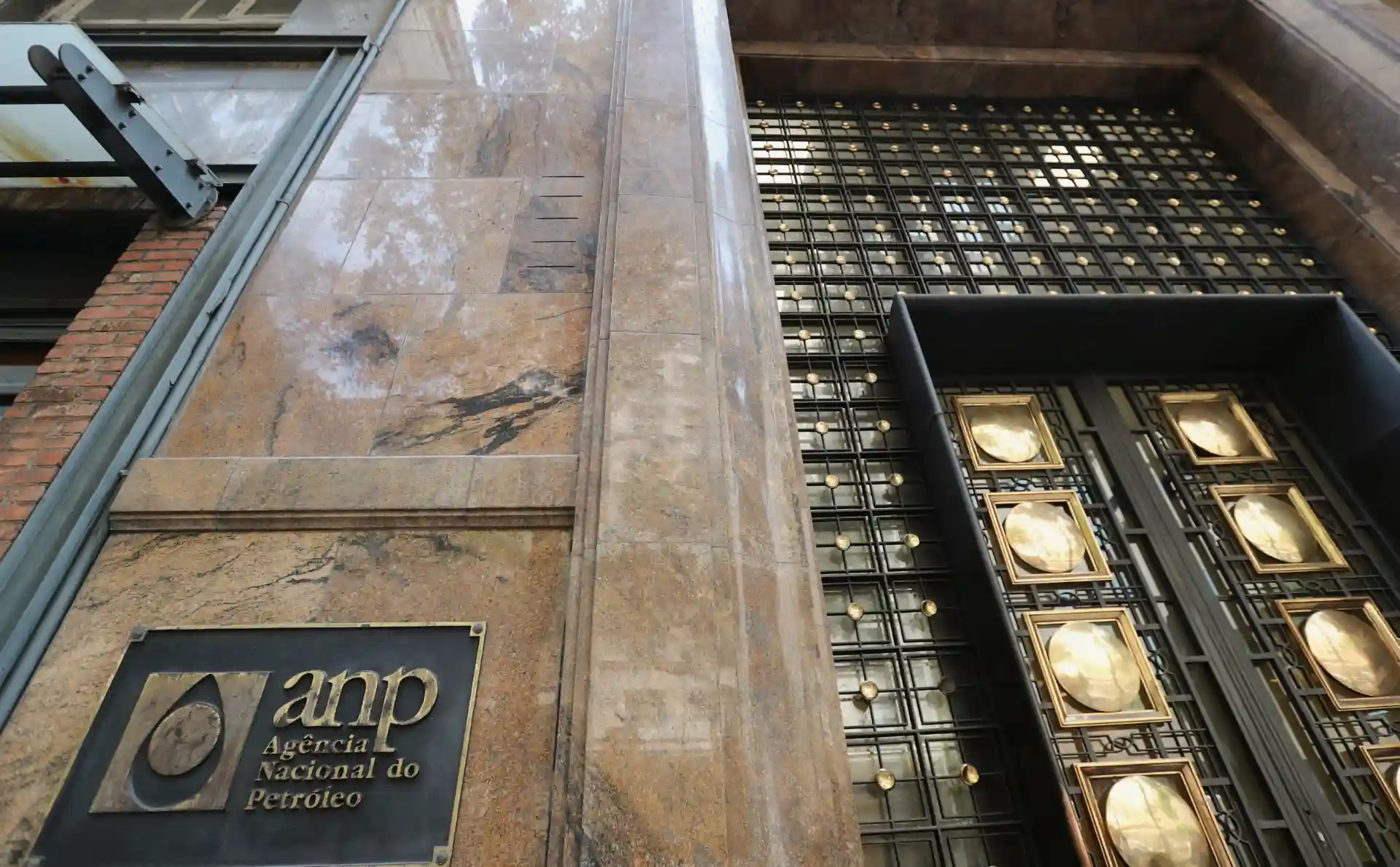 Imagem da fachada da Agência Nacional do Petróleo (ANP), com detalhes em mármore e um portão de metal com ouro, representando a importância do setor de petróleo no Brasil.
