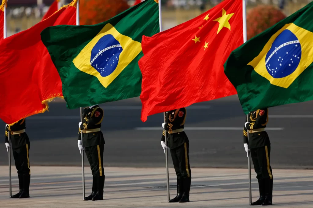Bandeiras do Brasil, China e outros países em desfile militar, destacando a importância das relações internacionais e parcerias entre países.