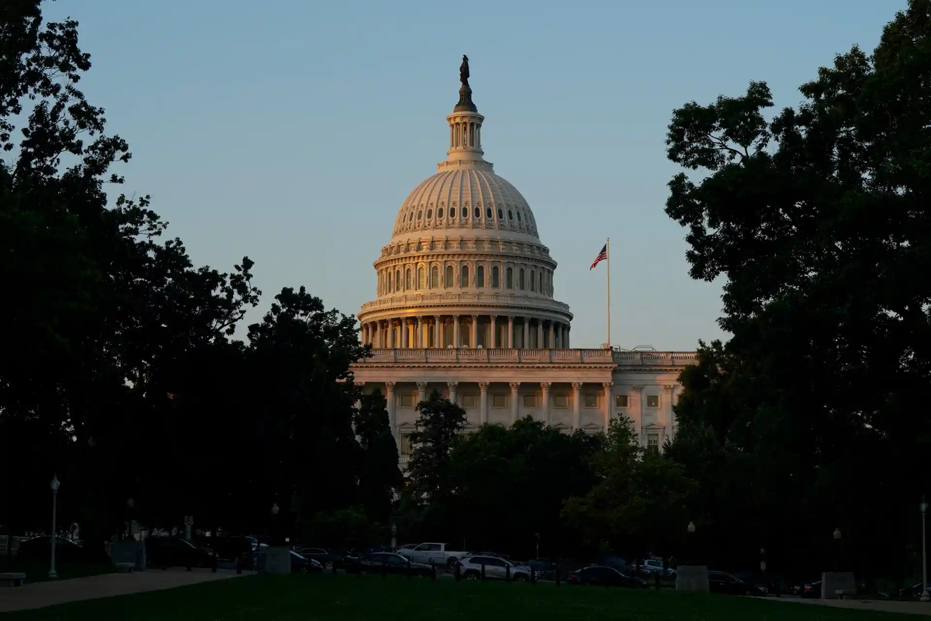 Imagem da Casa Branca em Washington, D.C., durante o pôr do sol, com árvores ao redor e céu claro ao fundo.