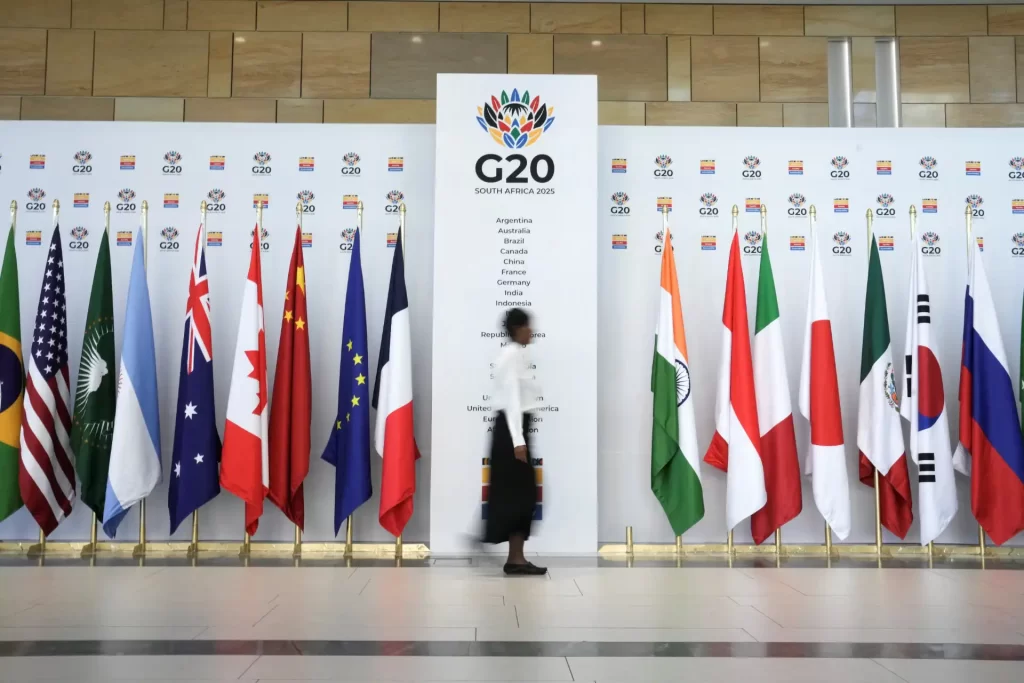 Pessoa andando por um corredor de bandeiras de diversos países na conferência G20 África do Sul 2023, promovendo a inclusão e diversidade mundial.