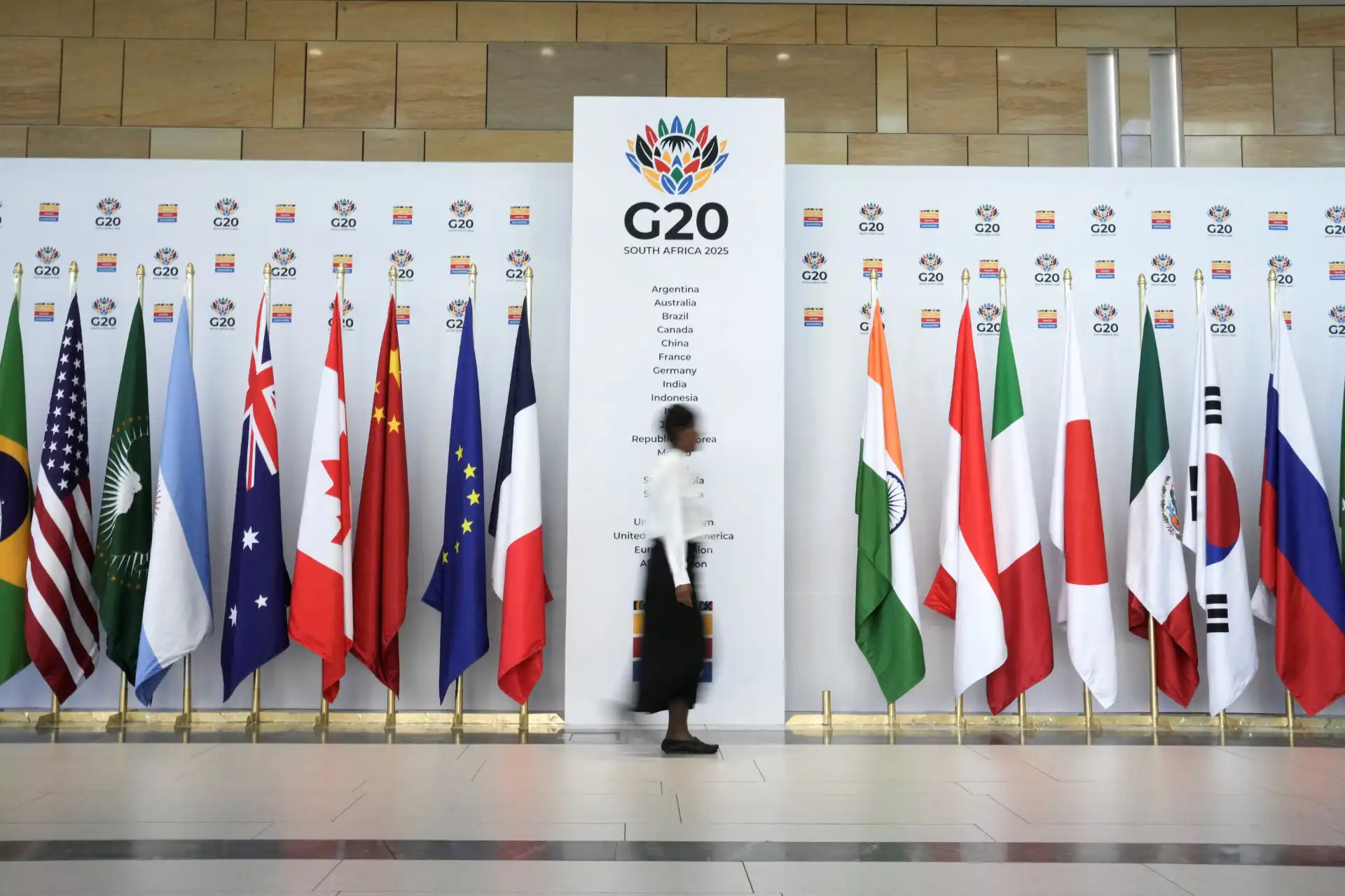 Pessoa andando por um corredor de bandeiras de diversos países na conferência G20 África do Sul 2023, promovendo a inclusão e diversidade mundial.