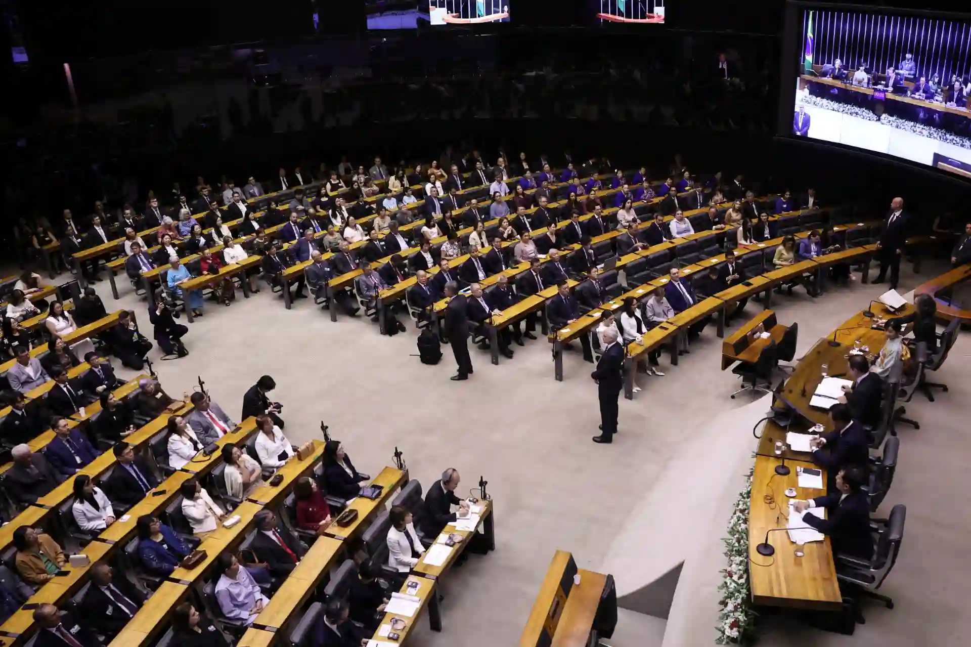 Reunião internacional de empresários e líderes mundiais em grande conferência, com participantes de diferentes países e um painel de oradores ao fundo.