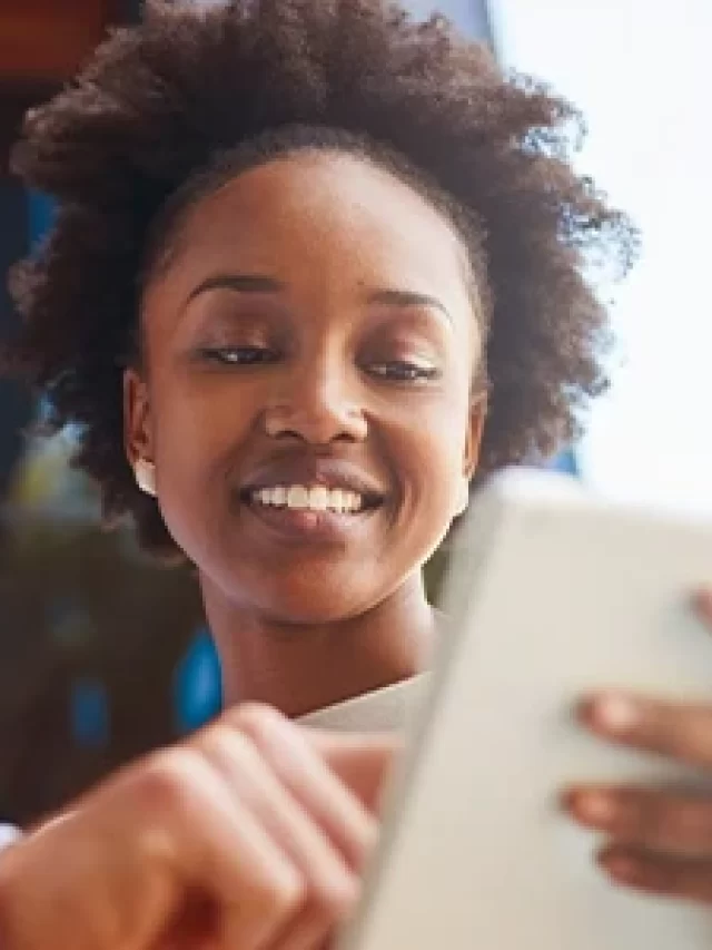 Story Homem e mulher sorrindo enquanto usam tablet, ambiente de escritório com prateleiras ao fundo, tecnologia e colaboração.