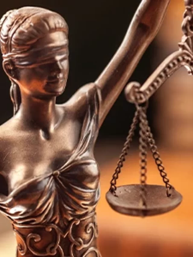 Imagem da escultura da Justiça com balança, simbolizando a imparcialidade e a equidade na área jurídica, sobre fundo de tribunal ou escritório de advocacia.