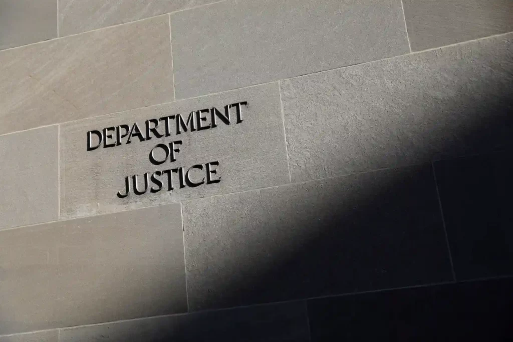 Imagem da fachada do Department of Justice com letras em relevo visíveis na parede de pedra de cor cinza.