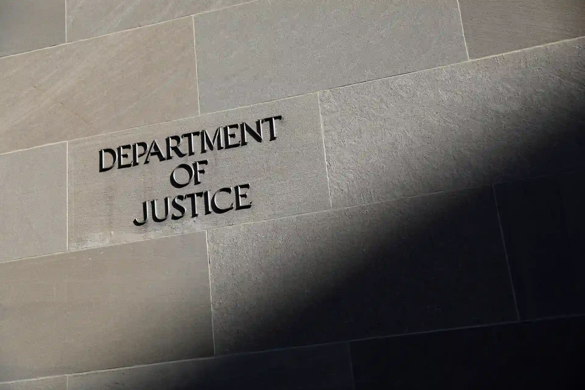 Imagem da fachada do Department of Justice com letras em relevo visíveis na parede de pedra de cor cinza.