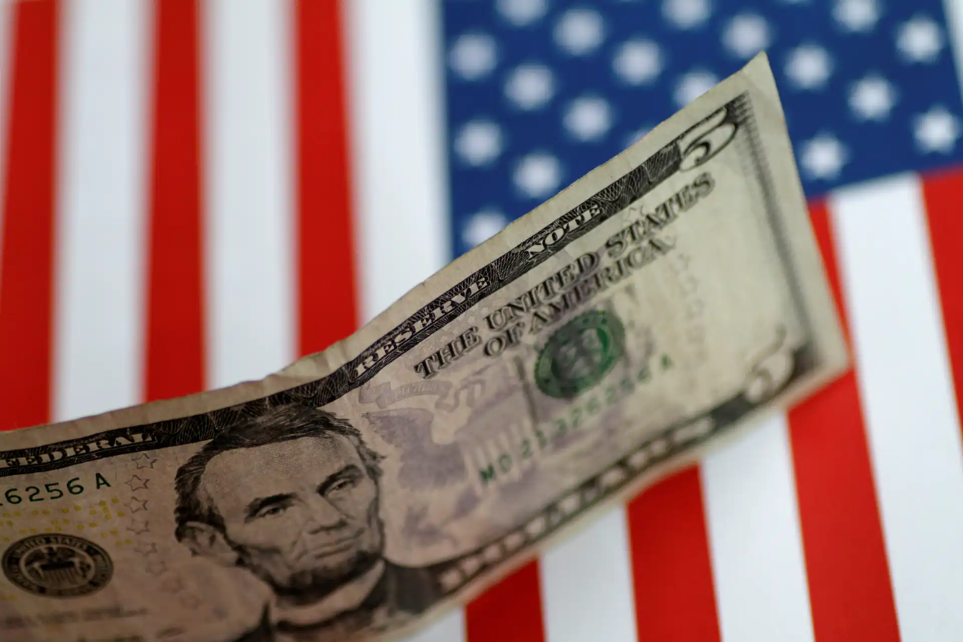 Dólar de 5 dólares em destaque, com fundo de bandeira dos Estados Unidos e cores vermelha, branca e azul.