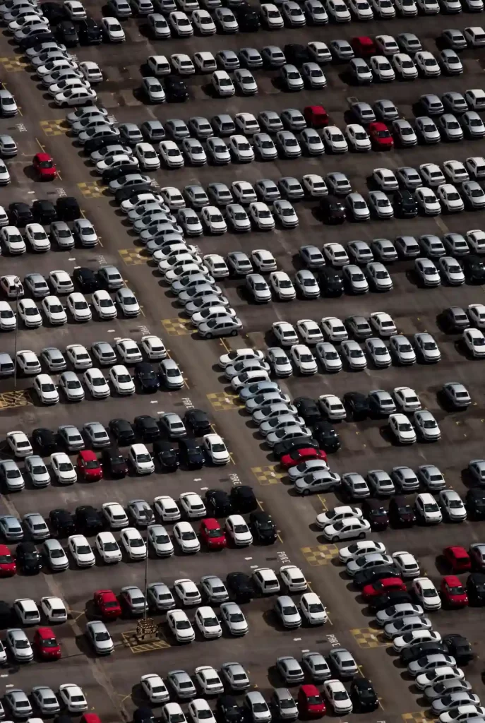 Estacionamento com muitos carros brancos, pretos e vermelhos em um grande pátio de estacionamento ao ar livre, organizado em filas e espaços demarcados
