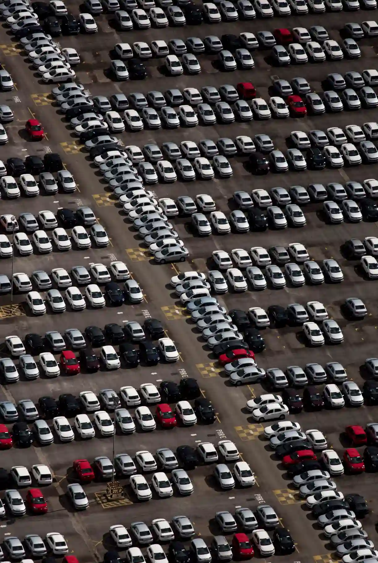 Estacionamento com muitos carros brancos, pretos e vermelhos em um grande pátio de estacionamento ao ar livre, organizado em filas e espaços demarcados