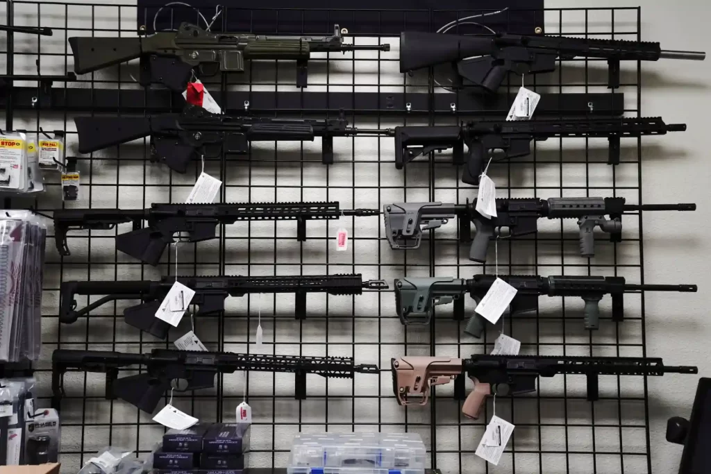 Exposição de armas de fogo variadas em uma loja, incluindo rifles de diferentes tamanhos e cores, organizados pendurados em uma grade de parede.