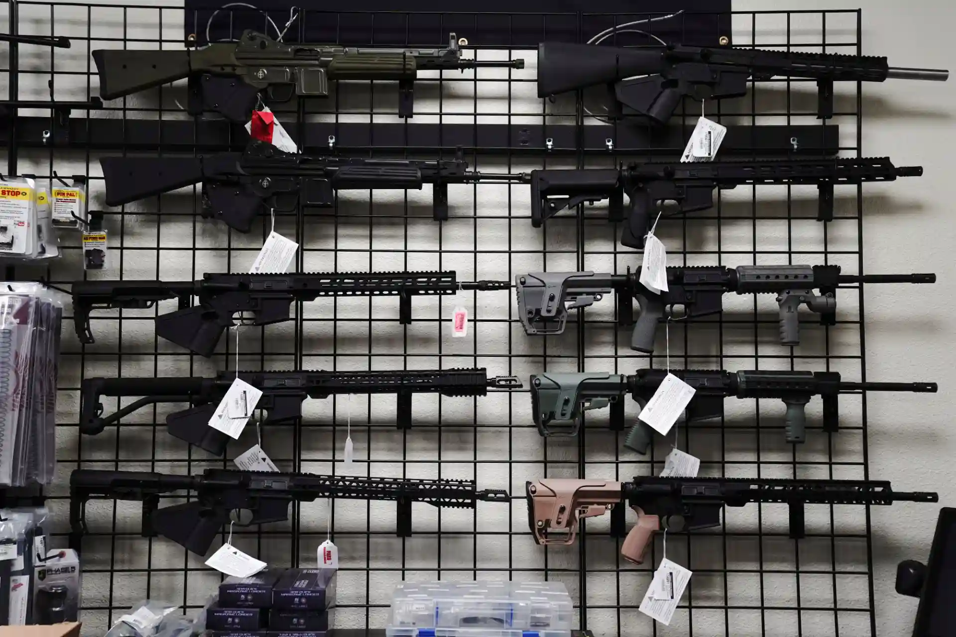 Exposição de armas de fogo variadas em uma loja, incluindo rifles de diferentes tamanhos e cores, organizados pendurados em uma grade de parede.