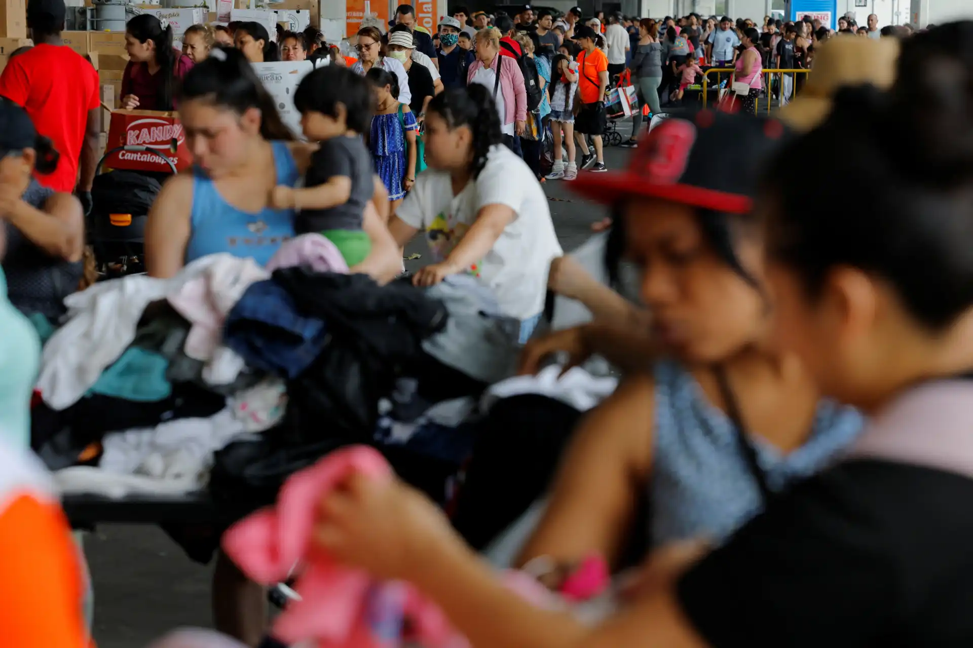 Diversas pessoas, incluindo crianças e adultos, em uma fila de espera em um ambiente público, possivelmente em um evento ou grande movimentação de pessoas.