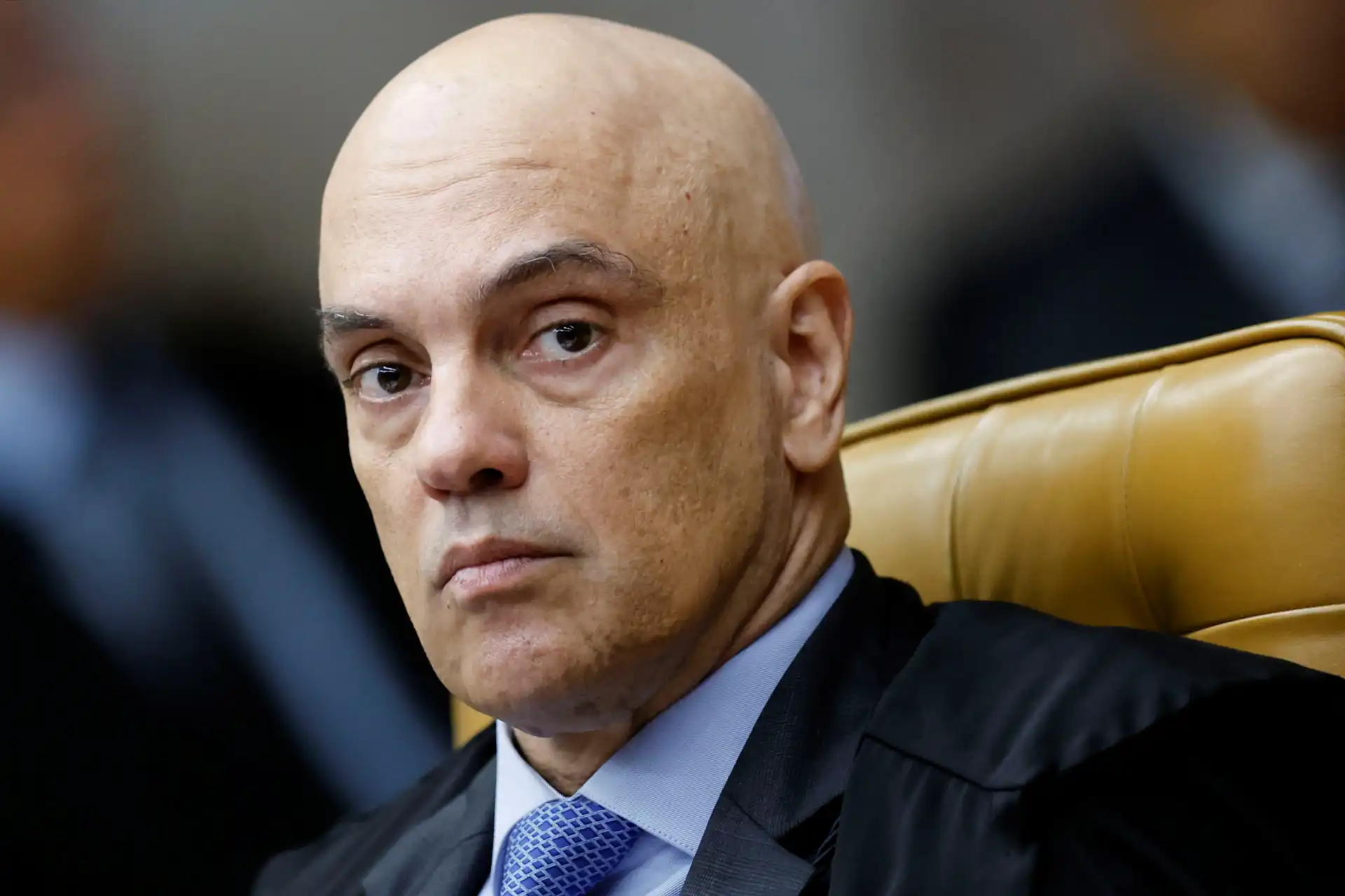 Imagem de uma pessoa séria em um ambiente formal, possivelmente um tribunal ou escritório de advocacia, com expressão de concentração.