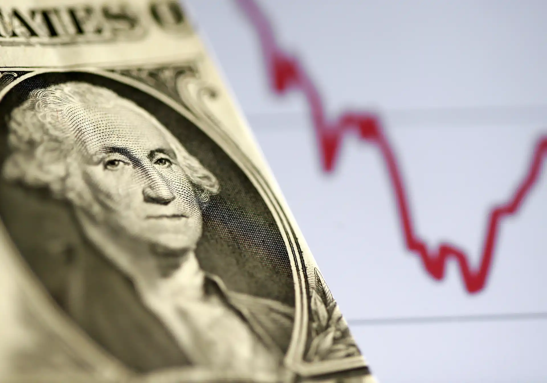 Imagem de uma nota de dólar com o retrato de George Washington ao lado de um gráfico financeiro em queda, simbolizando economia ou mercado financeiro.