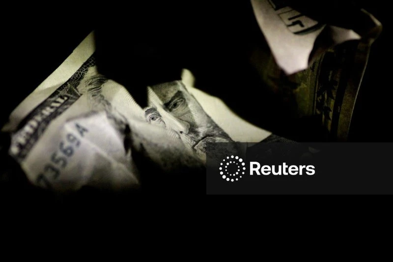 Imagem de uma nota de dólar sendo manipulada, destacando detalhes da cédula e a face de Benjamin Franklin, simbolizando dinheiro e economia.