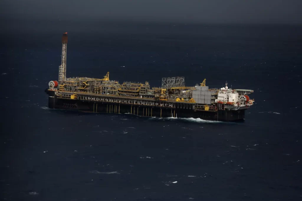 Platforma de petróleo no mar aberto, com estrutura industrial e ambiente marítimo, destacando-se na superfície do oceano em dia nublado.
