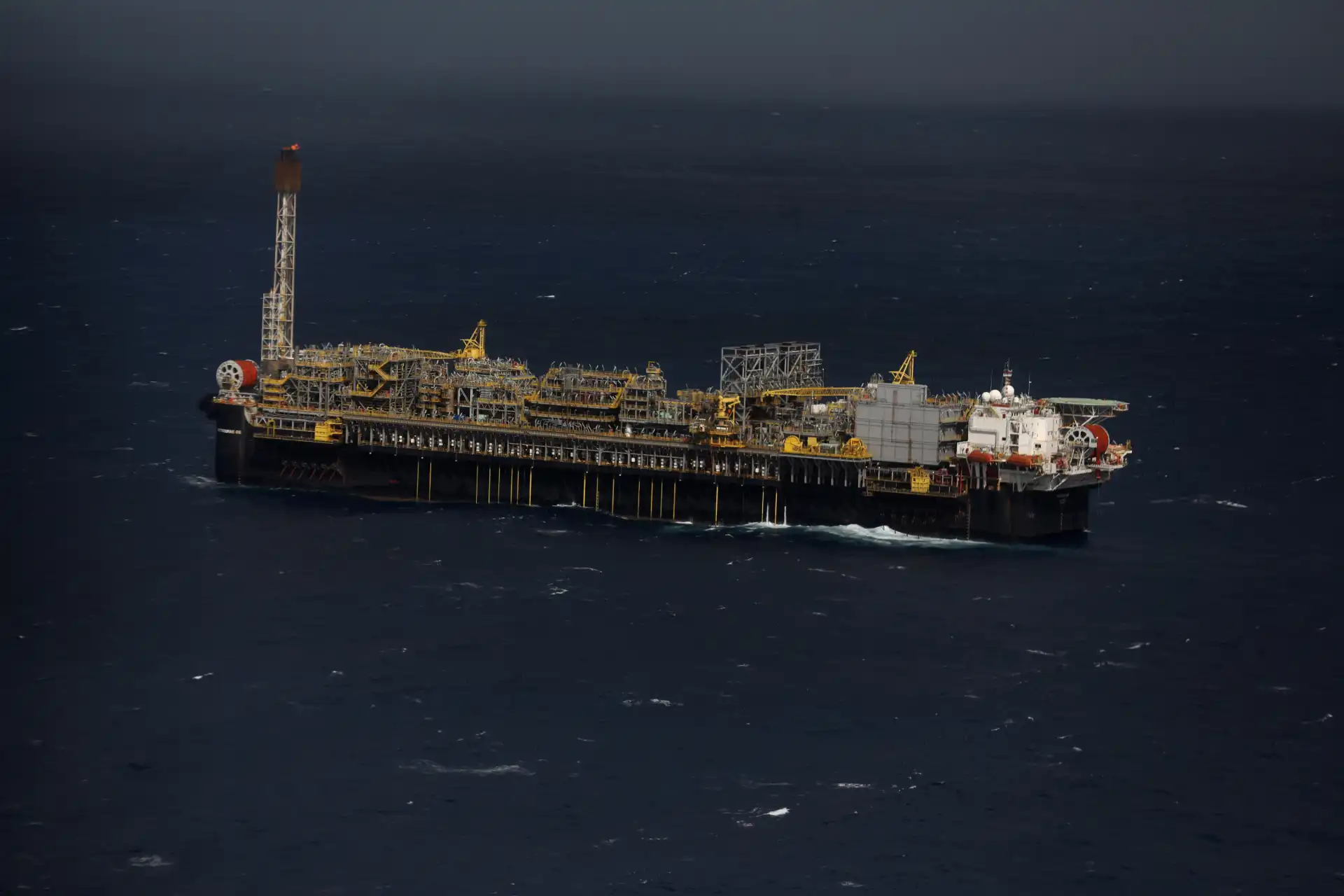 Platforma de petróleo no mar aberto, com estrutura industrial e ambiente marítimo, destacando-se na superfície do oceano em dia nublado.