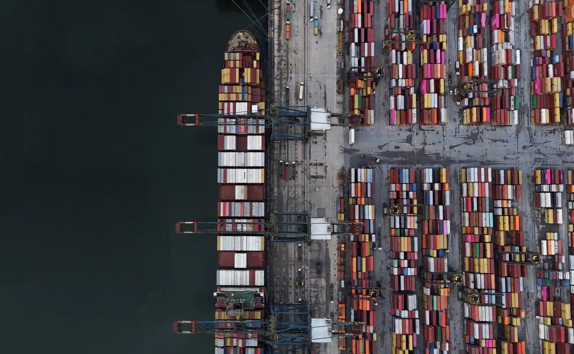 Imagem aérea de um porto de containers com barcos e guindastes, representando logística portuária e transporte marítimo.