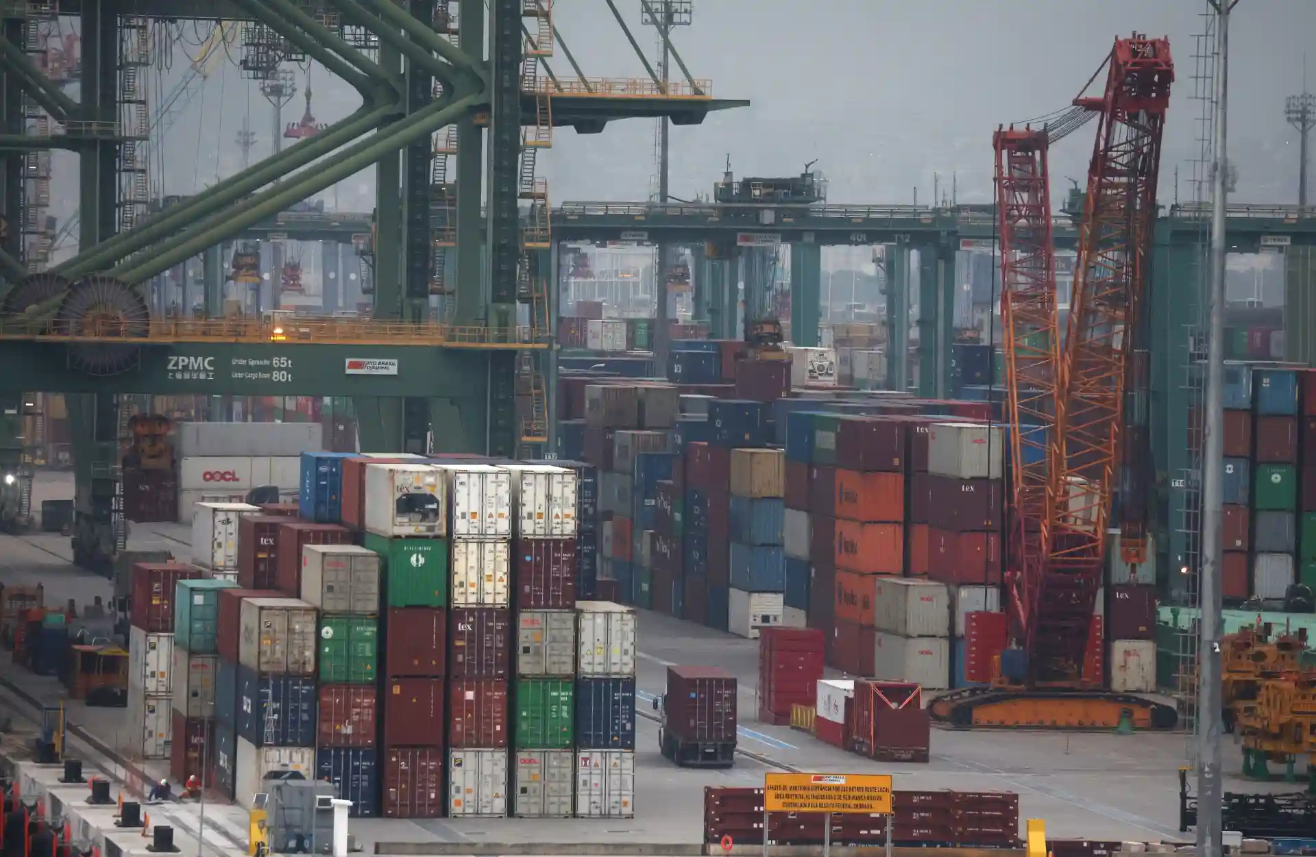 Imagem de um porto de containers com guindastes e várias cargas empilhadas, mostrando uma operação de transporte marítimo e logística.