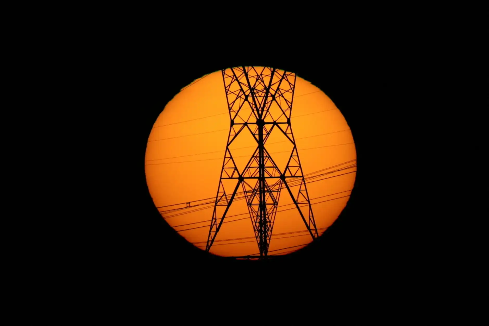Vista de uma torre de transmissão elétrica em silhueta contra um pôr do sol de fundo dourado.