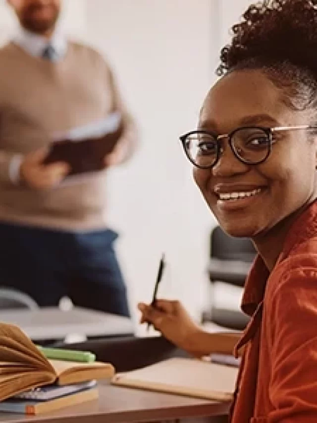 Aluno sorridente em sala de aula de escola, com colegas estudando ao fundo, ambiente de aprendizado positivo e motivador, ideal para destacar educação de qualidade.