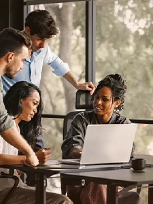 Equipe de profissionais de escritório colaborando em torno de uma mesa com computador portátil em ambiente moderno de escritório, promovendo trabalho em equipe e inovação e direito ao cuidado