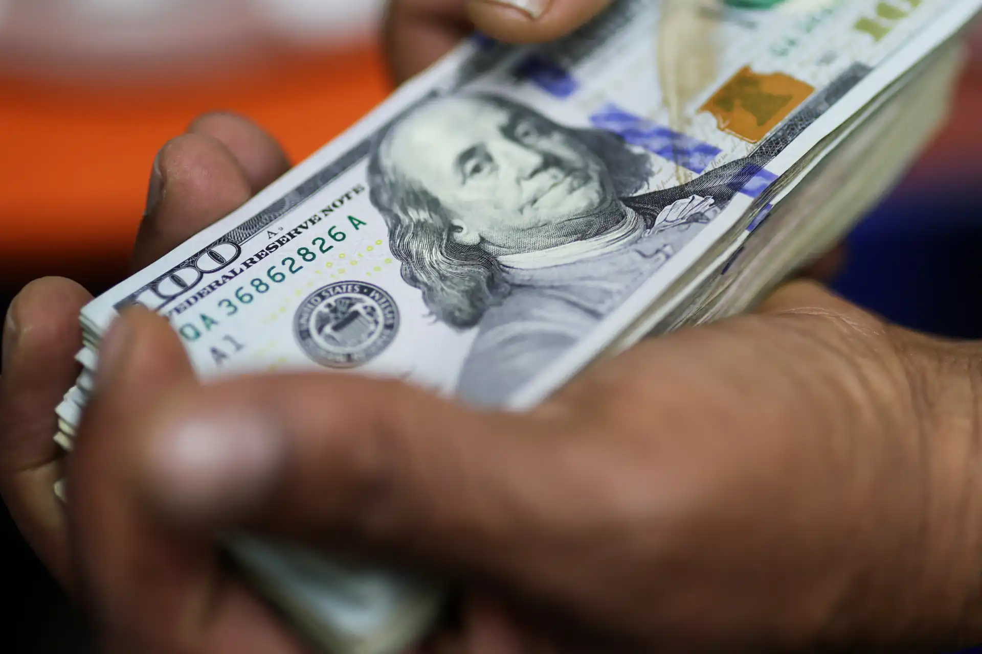 Mão segurando várias notas de dinheiro de 100 dólares americanos, com foco na nota de Benjamin Franklin, símbolo de riqueza e economia.