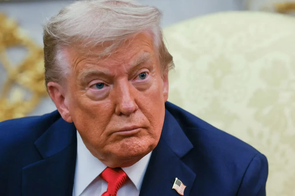 Imagem de Donald Trump, ex-presidente dos Estados Unidos, com expressão séria e vestindo um terno azul e gravata vermelha, em ambiente formal.