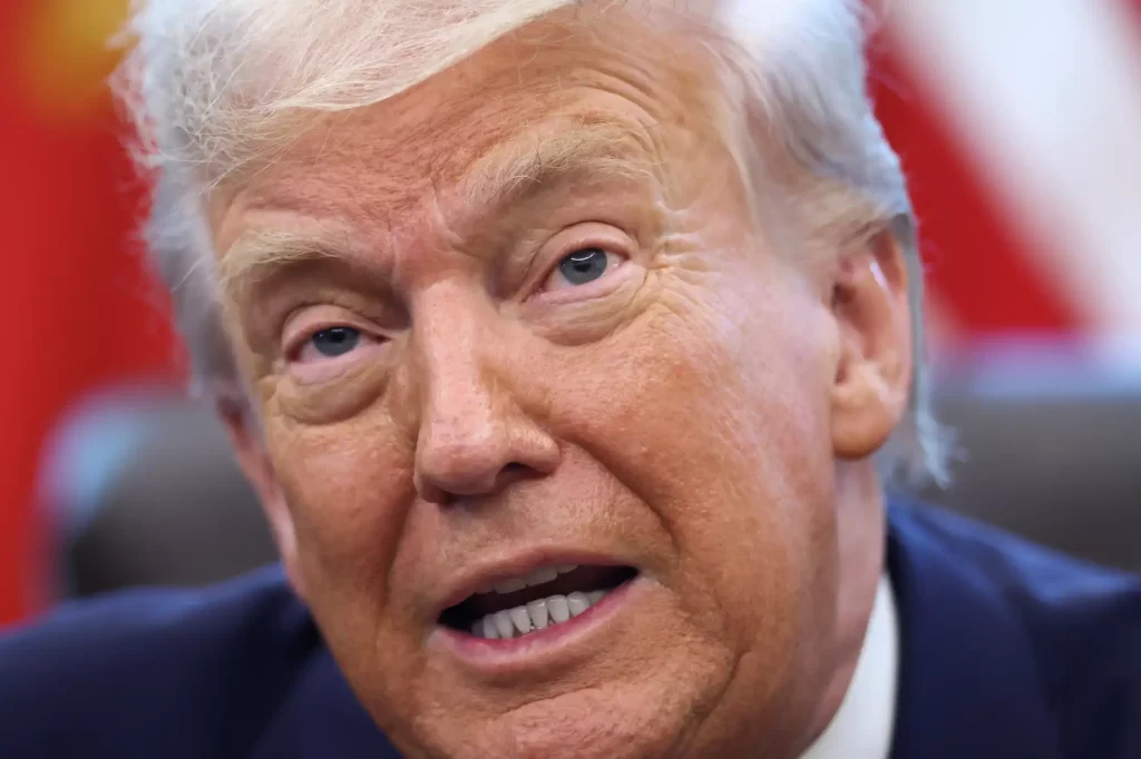 Imagem de Donald Trump, presidente dos Estados Unidos, fazendo uma expressão facial durante um evento político ou entrevista, com fundo desfocado.