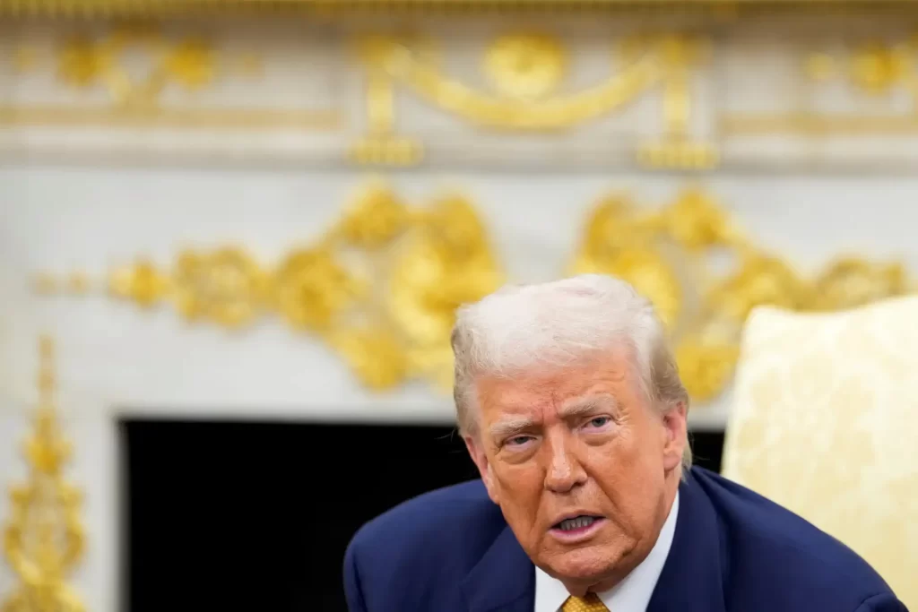 Imagem de Donald Trump em reunião, com expressão séria, fundo com detalhes dourados na parede, em destaque para assuntos políticos.
