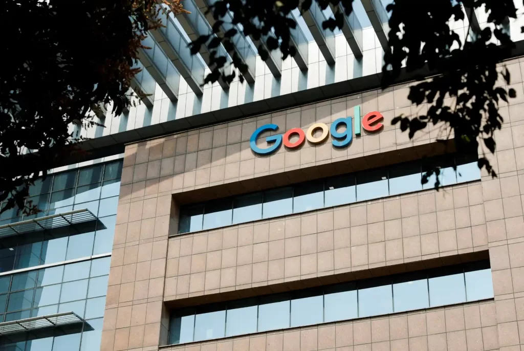 Imagem do edifício do Google com sua logomarca destaque na fachada, refletindo arquitetura moderna, escritório de tecnologia e inovação, e árvores ao redor.