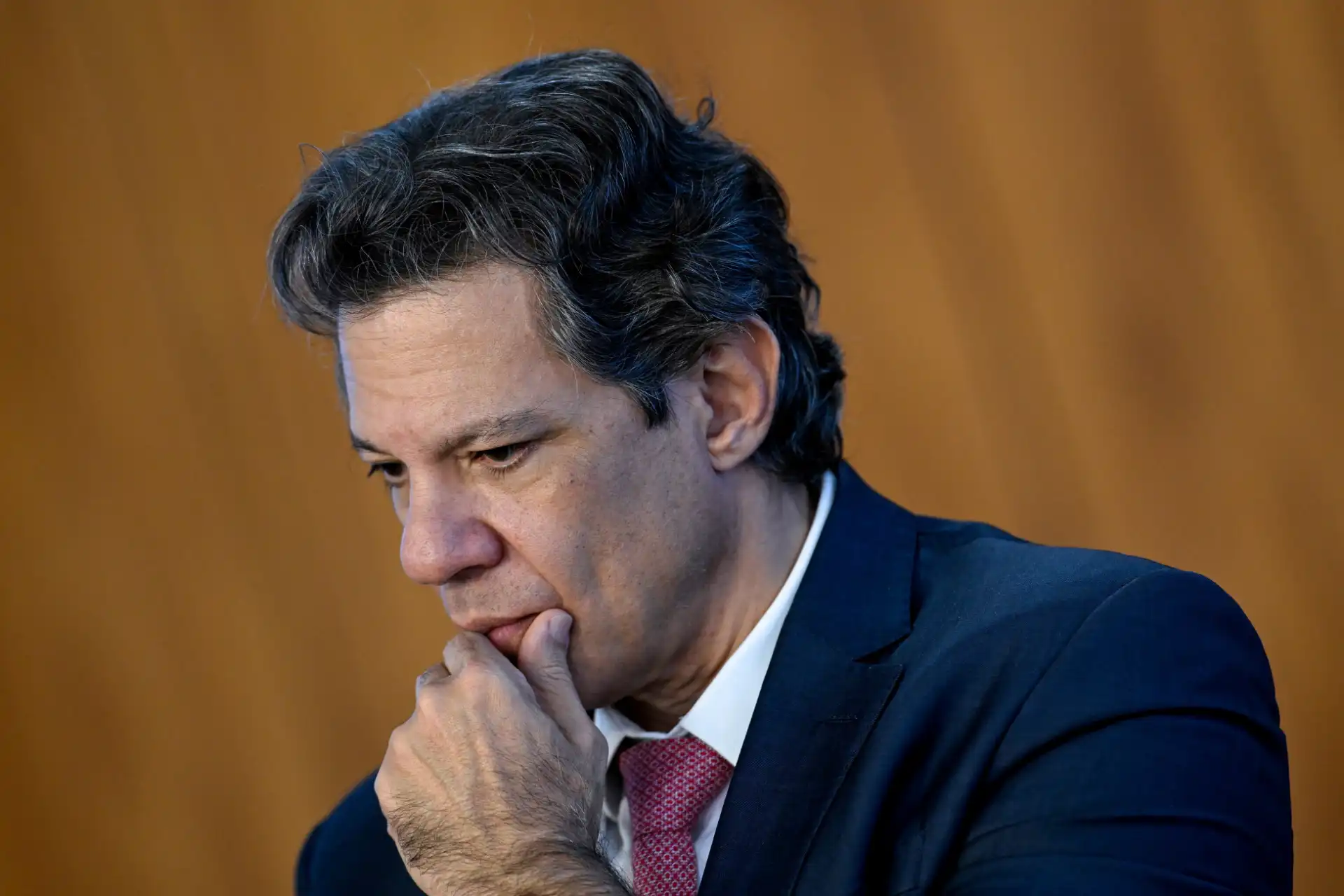imagem de homem pensativo com cabelo escuro e roupas formais, com fundo de tom alaranjado, representando reflexão ou análise.