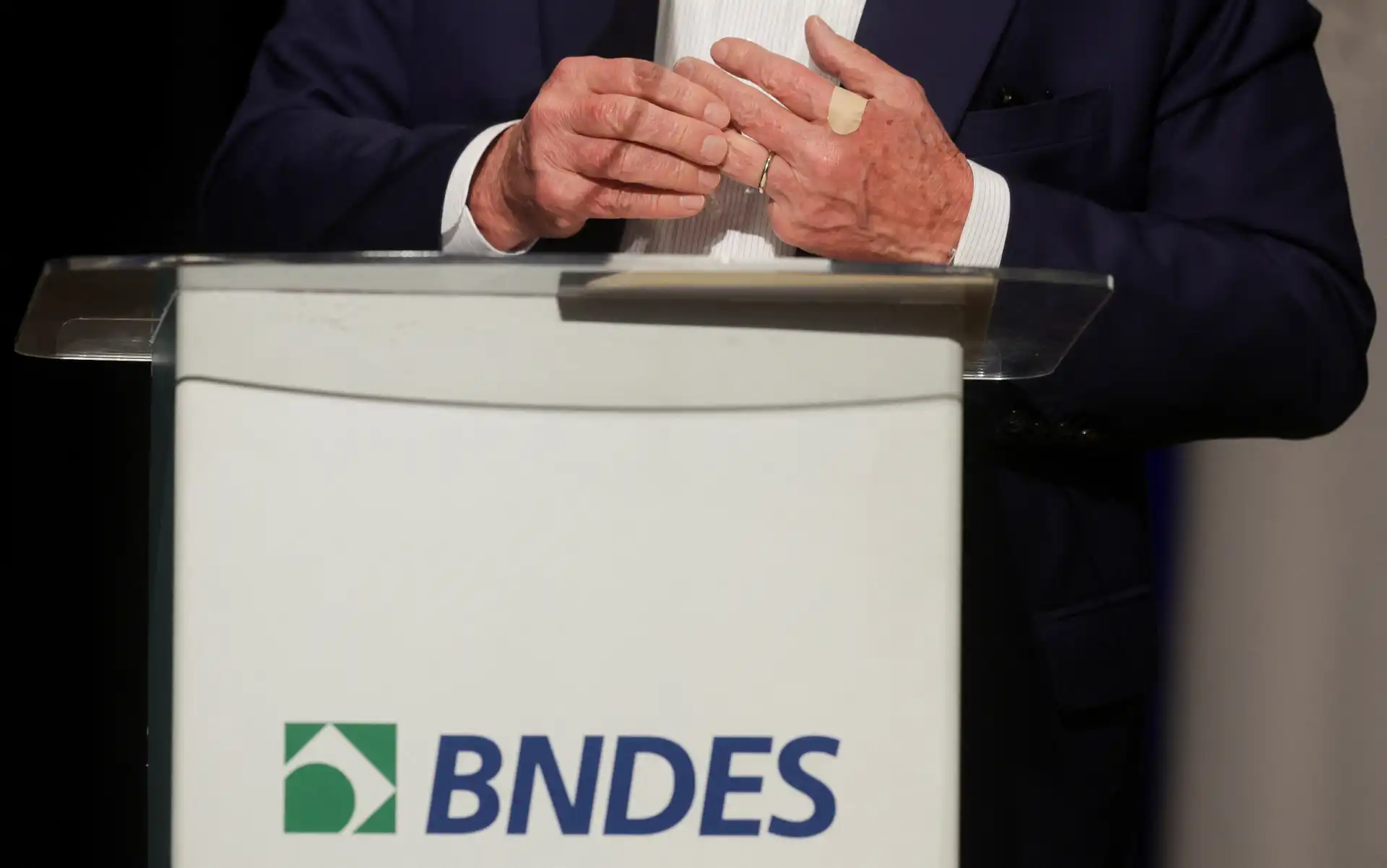 Homem vestindo terno na cerimônia de premiação, ao lado de um pódio com o logo do BNDES, durante evento oficial.