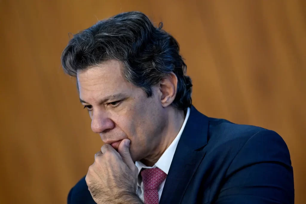 Imagem de um homem sério e pensativo, vestindo terno azul escuro e gravata rosa, com fundo de madeira, simbolizando reflexão ou concentração.