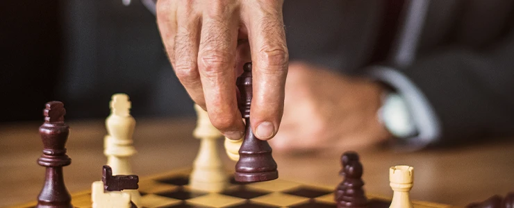 Homem jogando xadrez com foco na mão movendo uma peça no tabuleiro de xadrez para promover estratégias de jogo e raciocínio lógico. OAB