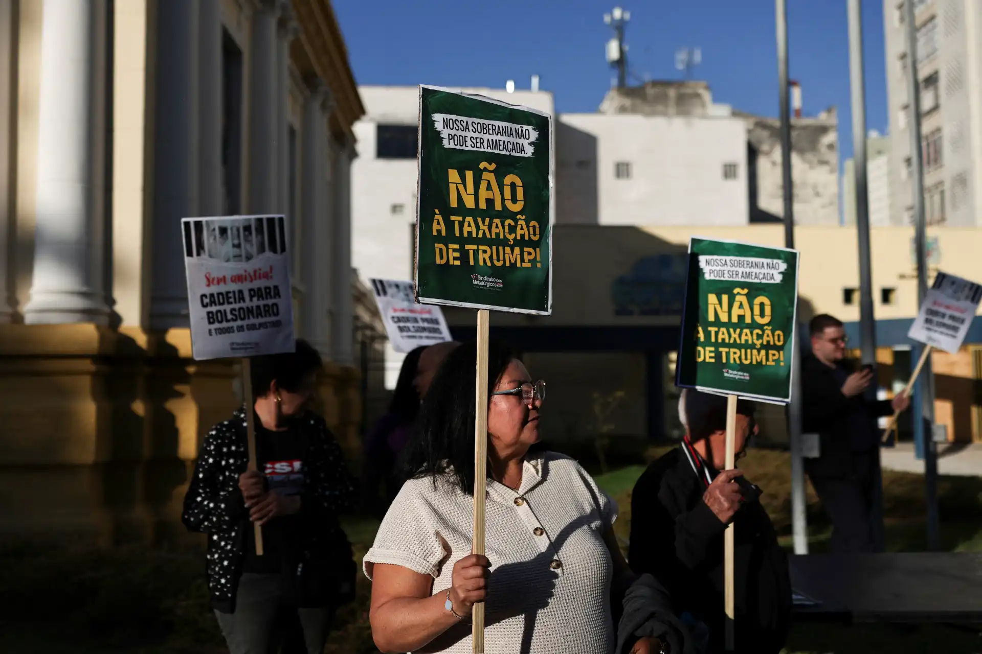 Manifestantes protestando contra a taxação de Trump, segurando cartazes com mensagens de resistência e questionamento da soberania nacional.