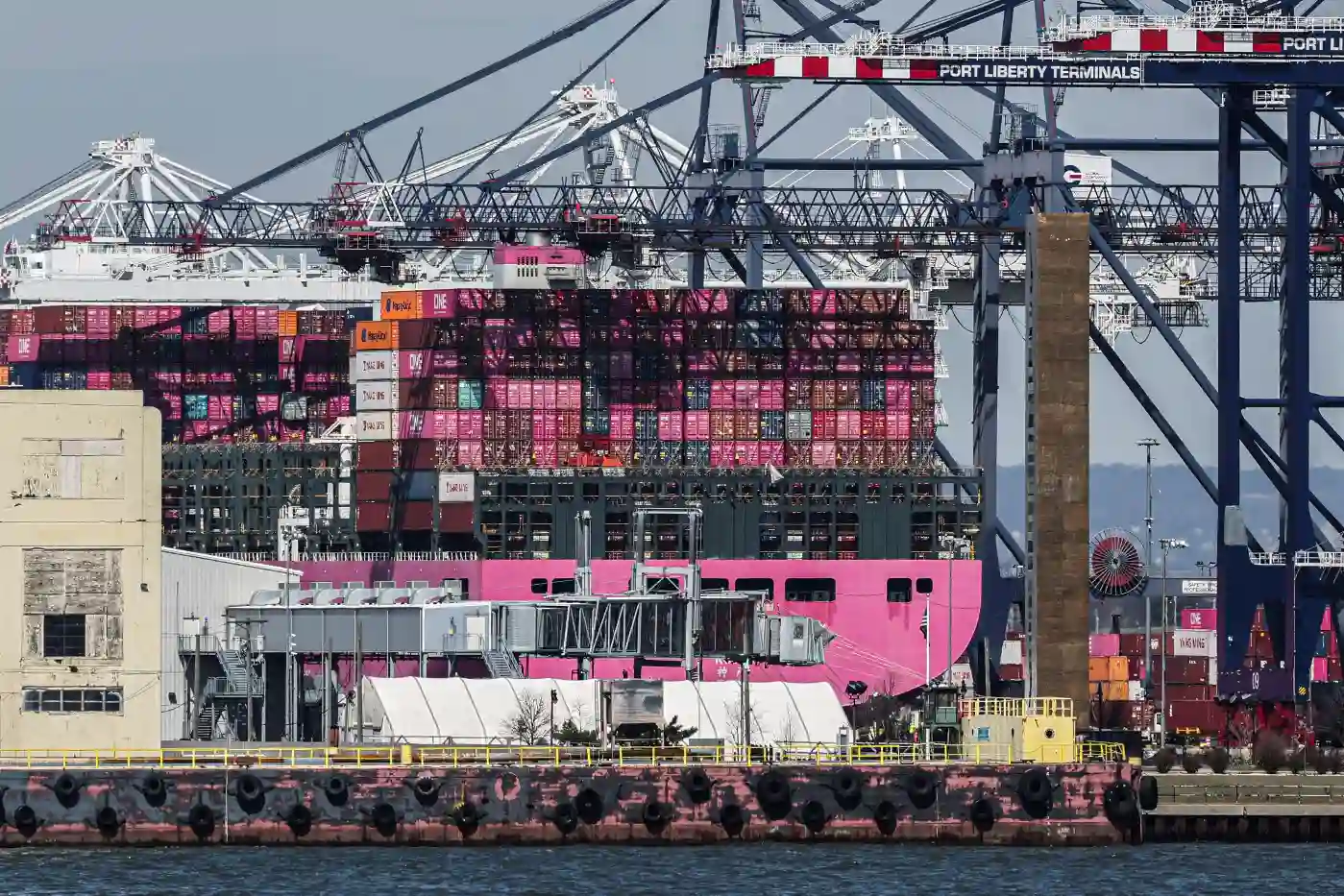 Imagem do porto de Los Angeles com contêineres coloridos, navios e guindastes em um cenário de transporte marítimo.
