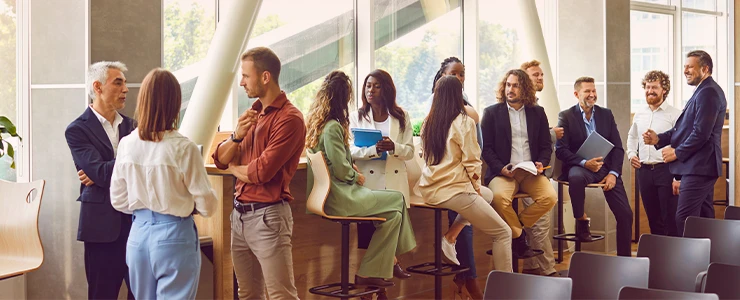 Grupo de pessoas em reunião de negócios ou treinamento corporativo em ambiente moderno de escritório, promovendo networking e troca de experiências.